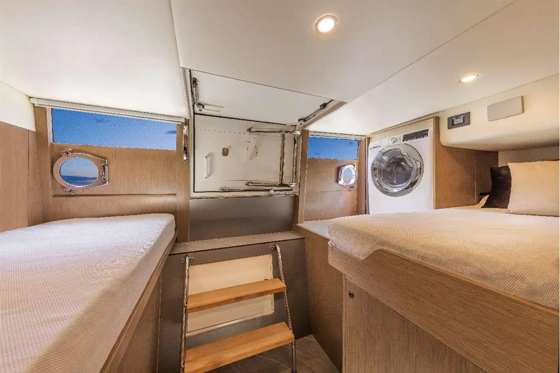 Bright, modern interior of a yacht cabin featuring two twin beds, a washing machine, and a scenic window view.